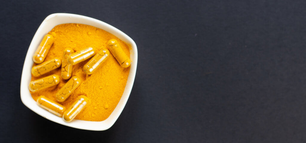 Top view of turmeric powder and capsules in a small white bowl on dark background Top view of turmeric powder and capsules in a small white bowl on dark background, which looks like DNP