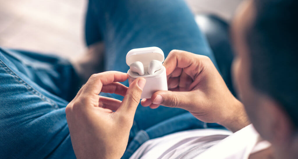 Wireless white headphones in the hands of a guy. Man holding Apple AirPods